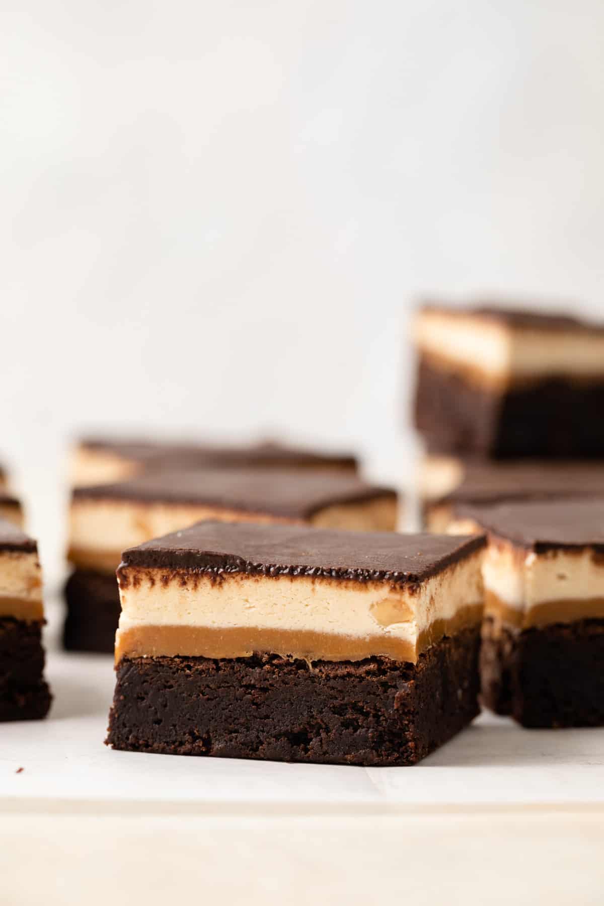A close up view of a fudgy chocolate brownie with layers of gooey caramel, chewy nougat, and chocolate ganache over the top.