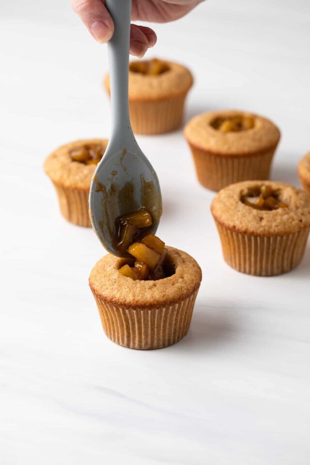 A spoon filling apple spice cupcakes with apple filling