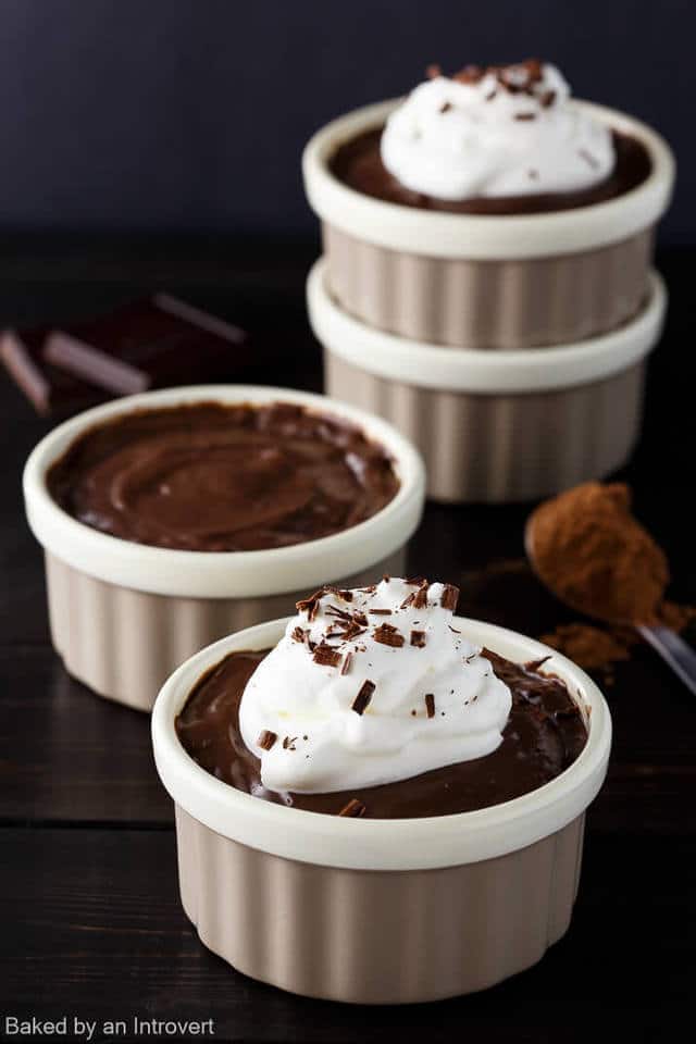 Angled view of chocolate pudding with whipped cream on top in a tan ramekin.