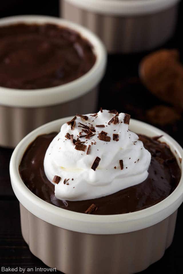 Close up angled view of chocolate pudding with whipped cream on top in a tan ramekin.