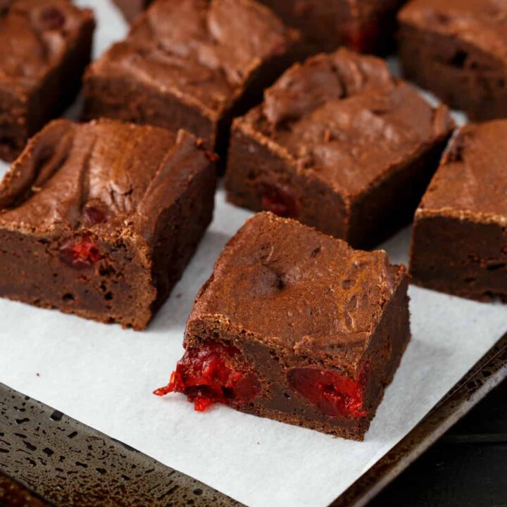 Chocolate cherry brownies on a baking sheet lined with white parchment paperl