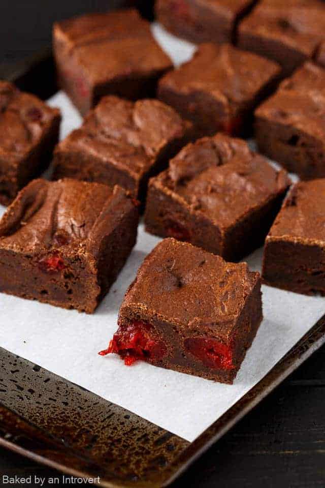 Chocolate cherry brownies on a baking sheet lined with white parchment paperl