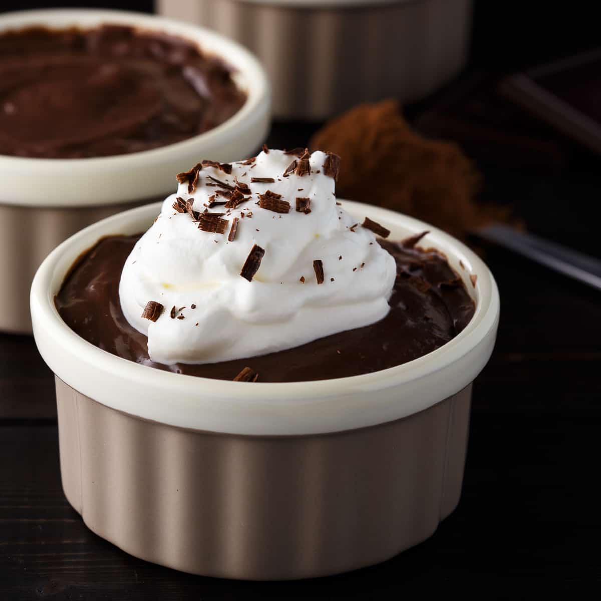 Side view of chocolate pudding with whipped cream on top in a tan ramekin.