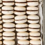 stacks of french macarons inside a baking pan with parchment paper