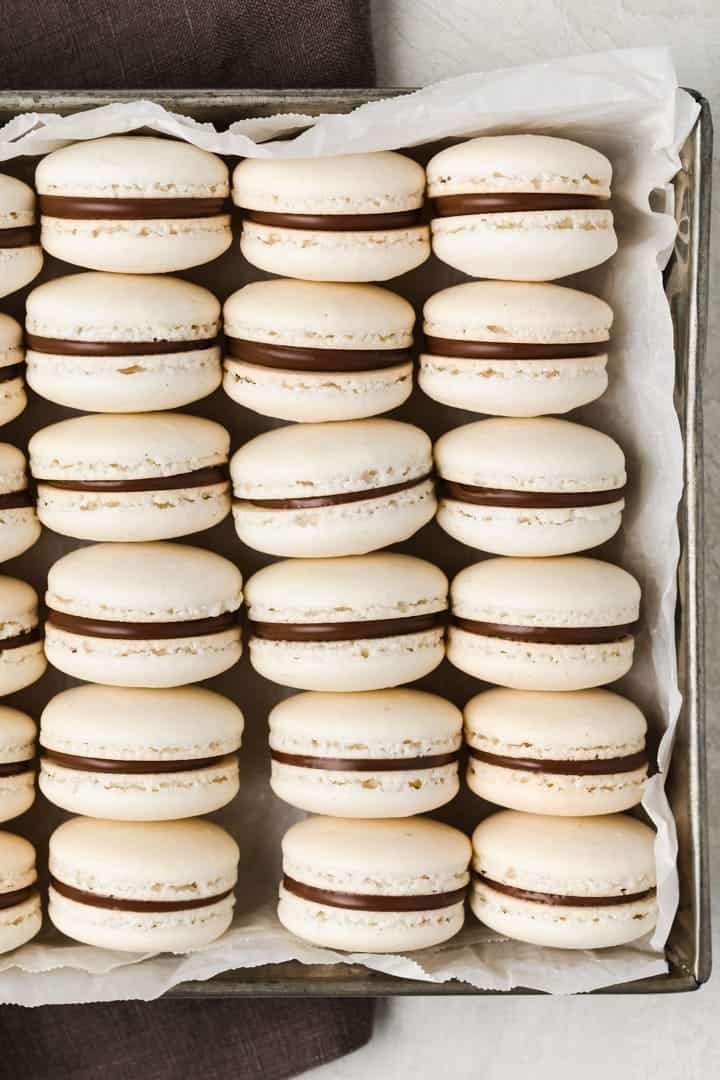 stacks of french macarons inside a baking pan with parchment paper