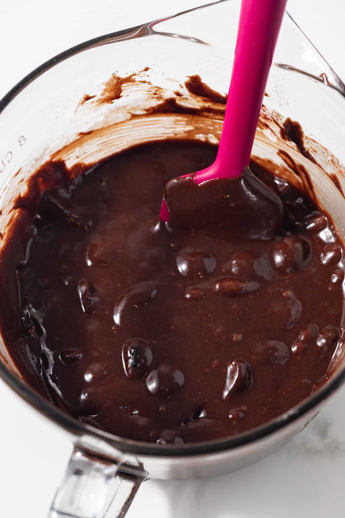 Chocolate cherry brownie batter in a glass bowl with spatula.