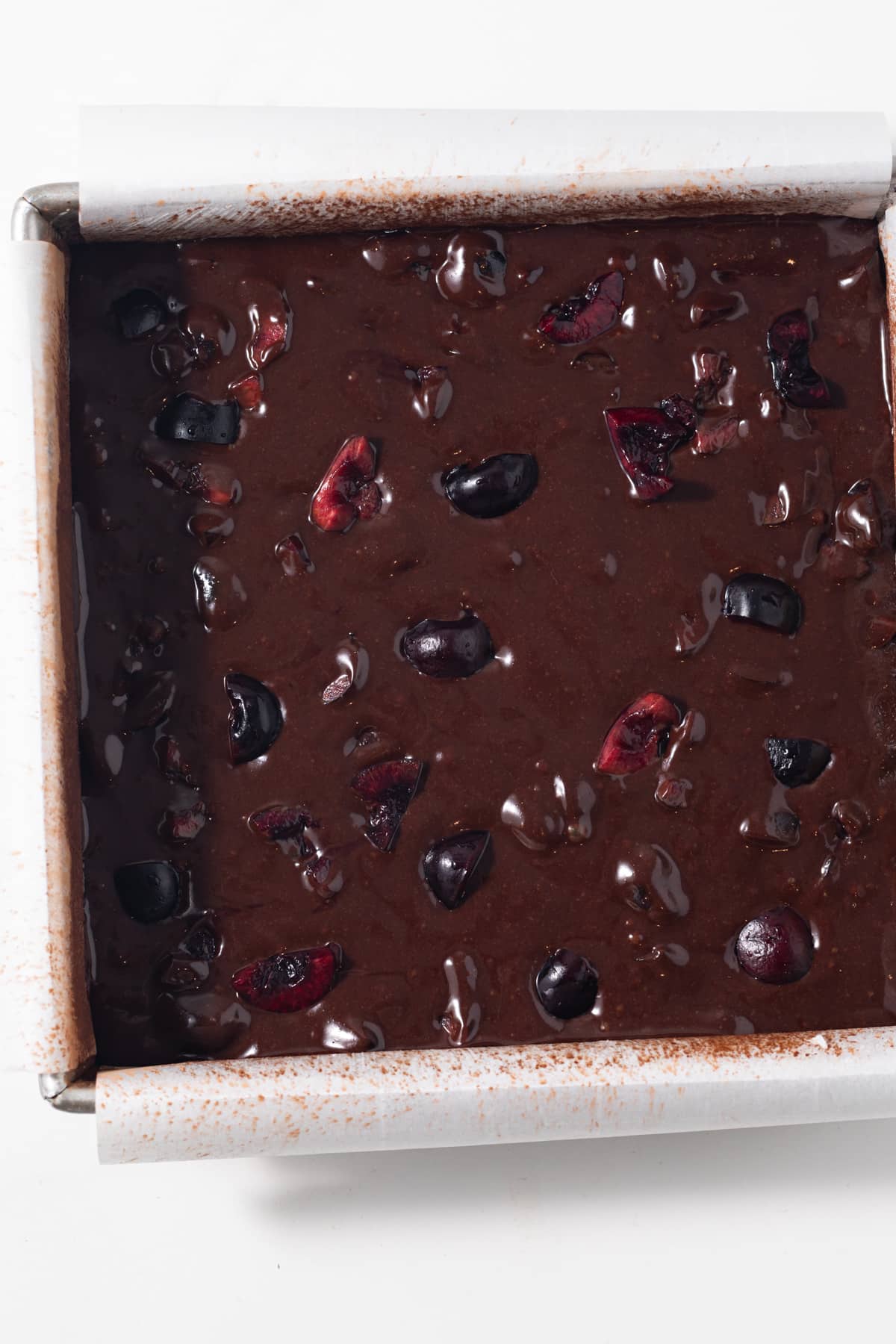 Unbaked brownie batter with cherries in a baking pan.
