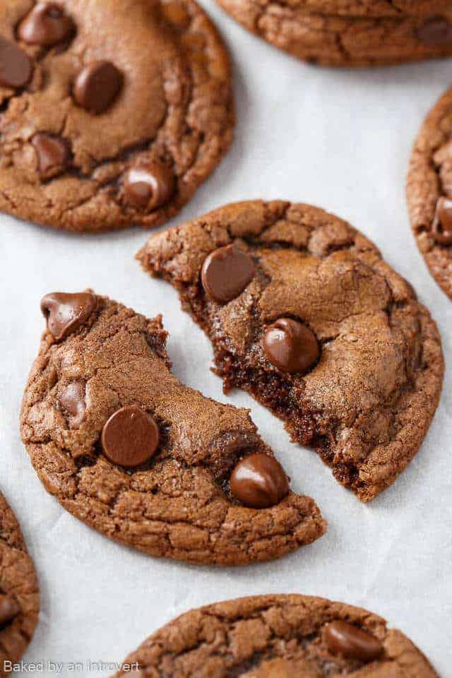 A Double Chocolate Chip Nutella Cookie broken in half on white parchment paper.