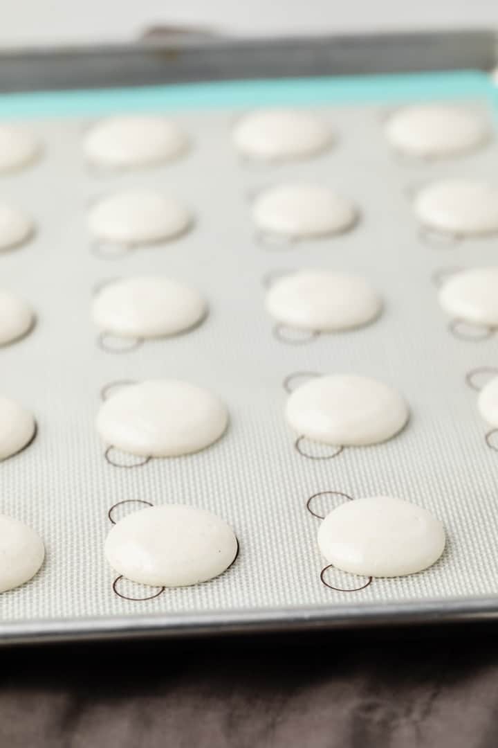 unbaked macaron shells on a baking sheet lined with a silicone mat