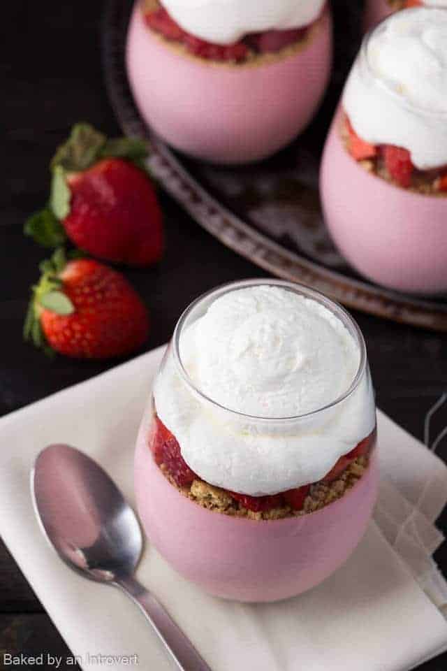 High angled view of strawberry cheesecake mousse in a glass jar on a cream napkin with a spoon.