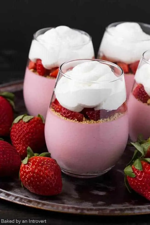 Strawberry cheesecake mousse in glass jars with strawberries scattered around.
