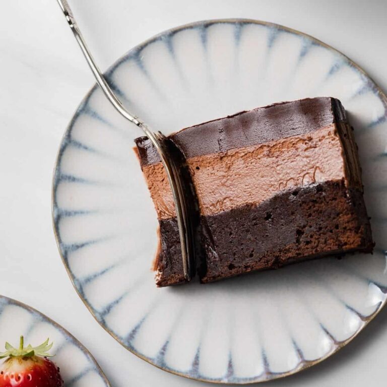 Slice of triple chocolate mousse cake on plate with fork taking a bite out.