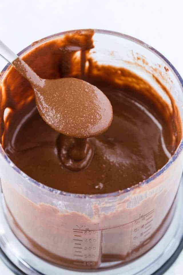 Smooth homemade nutella in the bowl of a food processor with a spoon being dipped in.