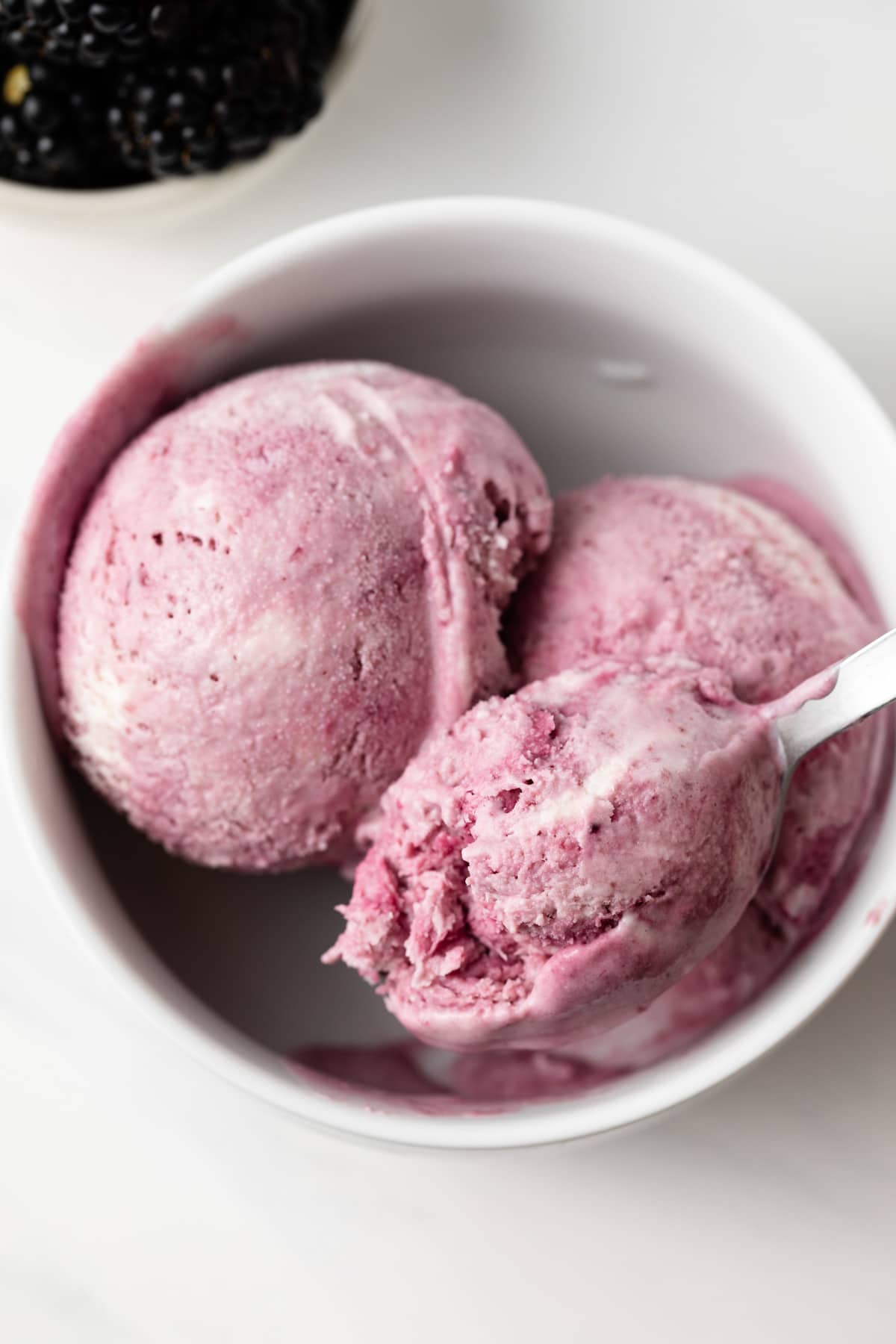 Spoon scooping out blackberry swirled ice cream.