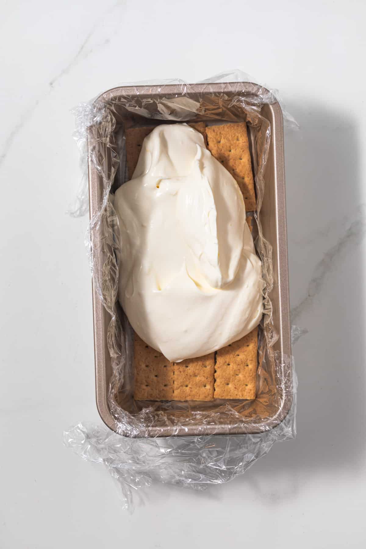 Lemon whipped cream layered over graham crackers in loaf pan.
