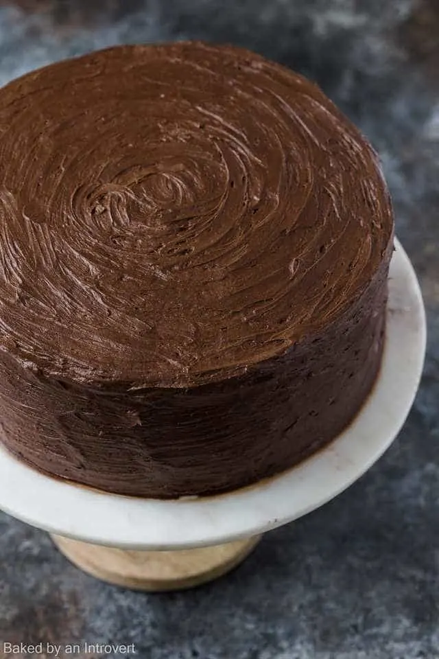 Angled view of a cake covered in chocolate frosting on a marble cake stand.