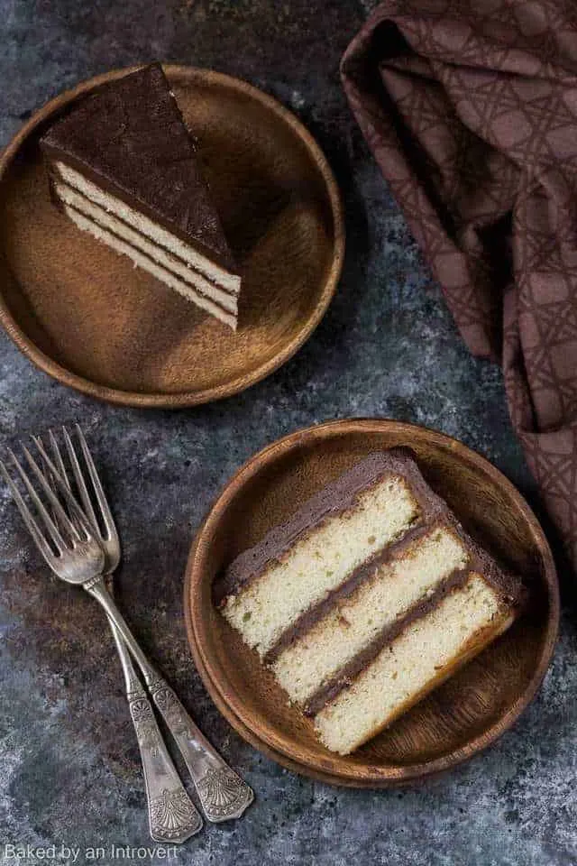 Overhead view of two slices of yellow cake with chocolate frosting on bamboo plates.