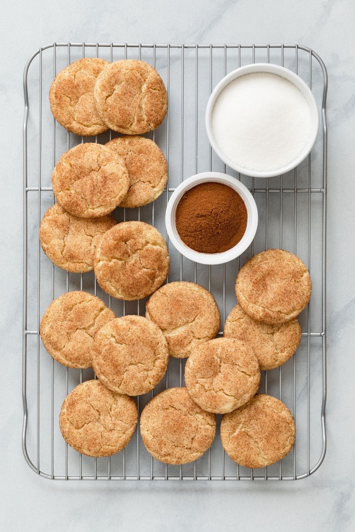 snickerdoodle cookies on wire rack with bowls of cinnamon and sugar