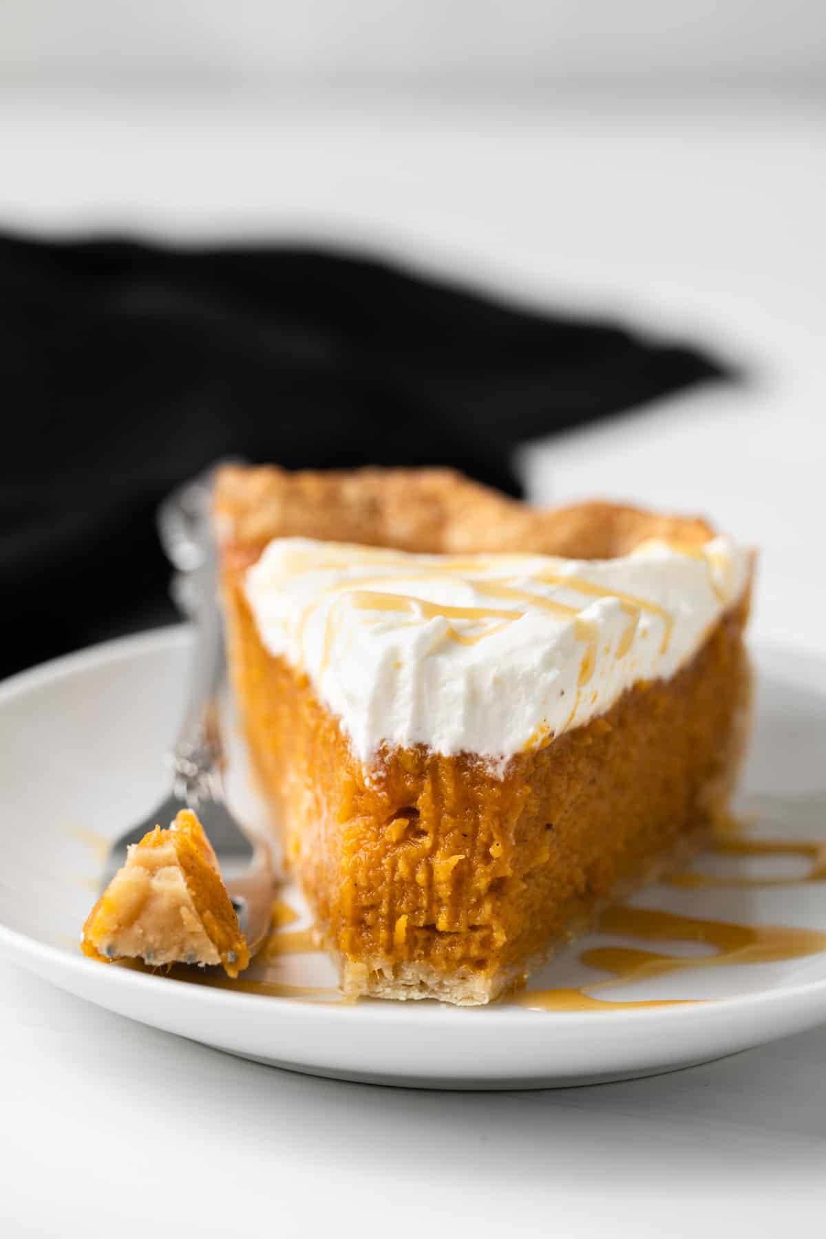 Slice of caramel sweet potato pie on a white plate with fork taking a bite out