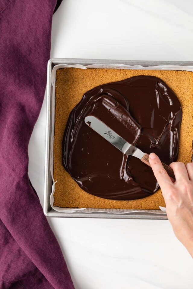 Melted chocolate being spread on top of graham cracker crust