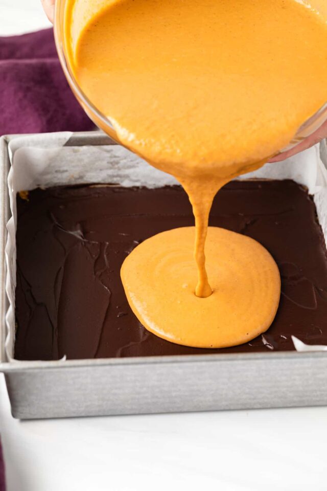 Pumpkin bar batter being poured onto a chocolate and graham cracker crust