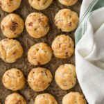 Bacon Garlic Gougères lined on a baking sheet with a cream and green cloth napkin to the side.