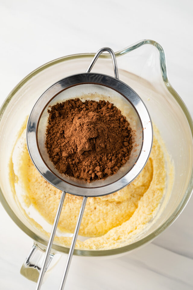 Cocoa powder and flour being sifted into an egg and sugar mixture