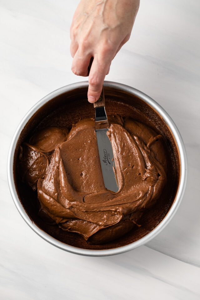A spatula spreading chocolate cake batter in a round pan