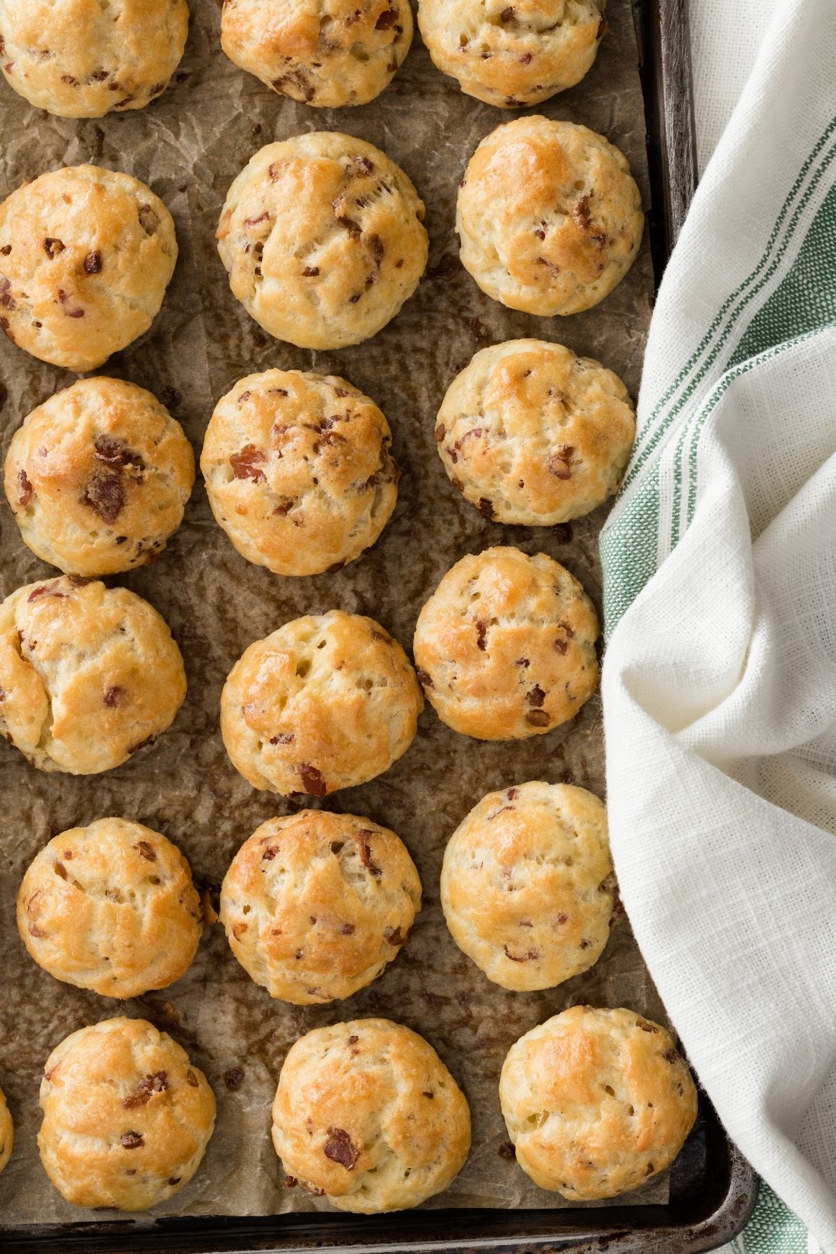 Bacon Garlic Gougères lined on a baking sheet with a cream and green cloth napkin to the side.