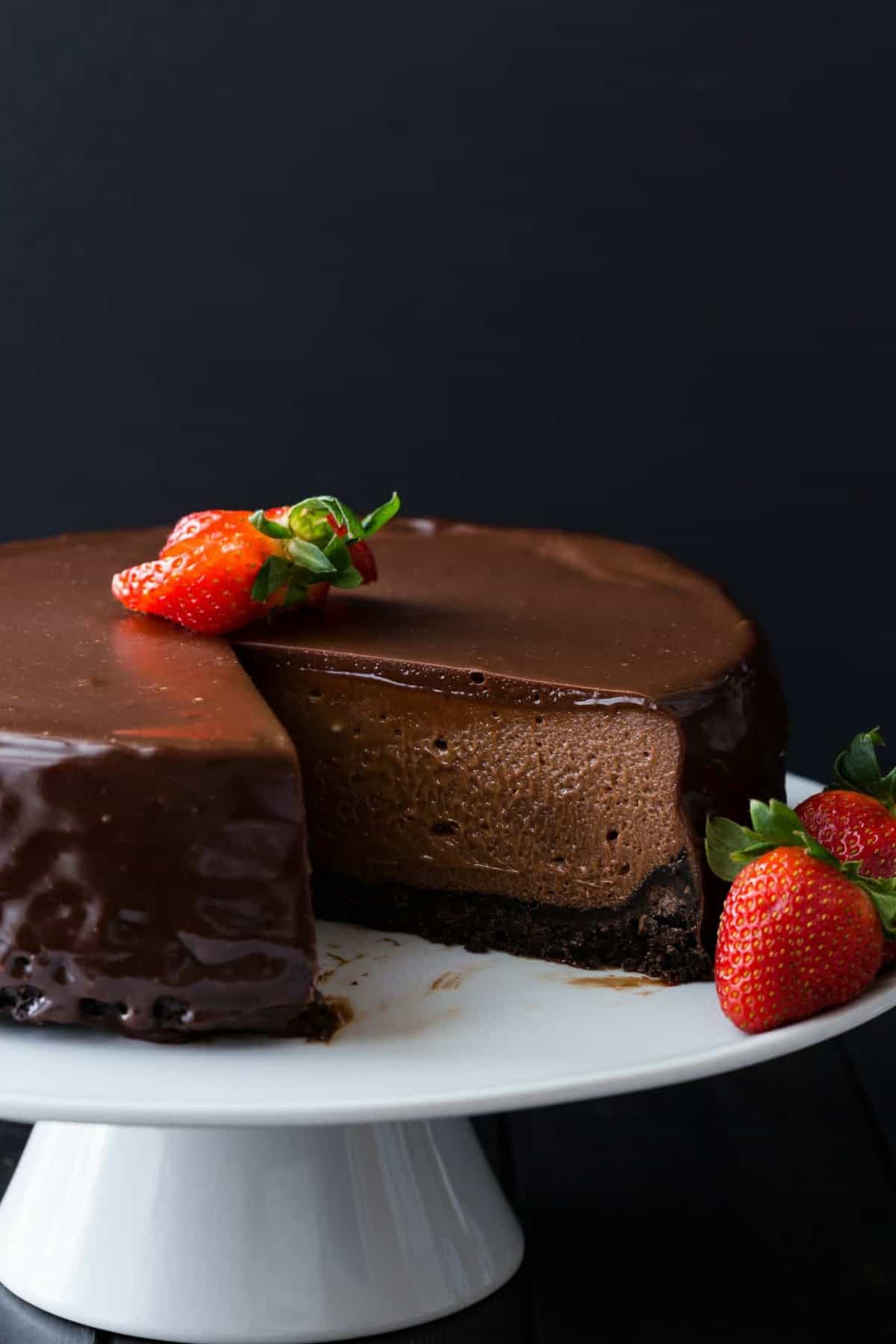 Nutella cheesecake topped with fresh strawberries on a white cake stand with a slice taken out.