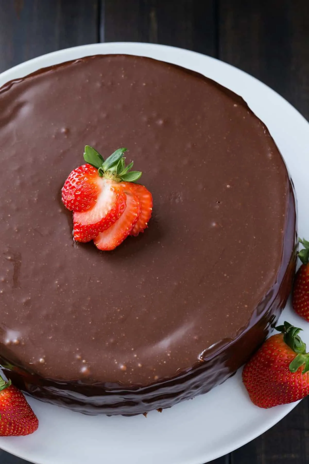 Nutella cheesecake covered in nutella glaze topped with fresh strawberry slices on a white serving platter.