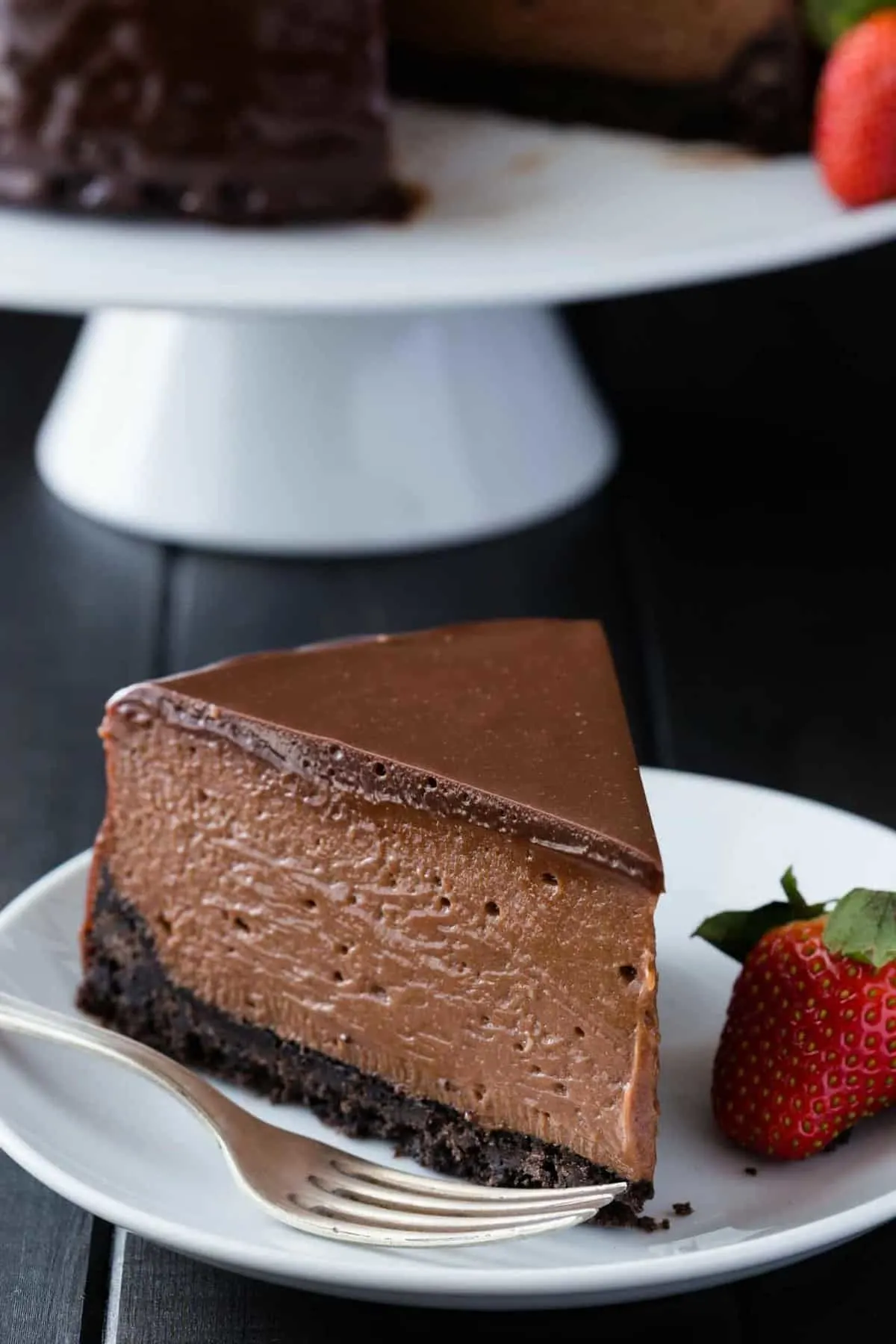 A slice of creamy nutella cheesecake on a white plate with a strawberry sitting next to it.