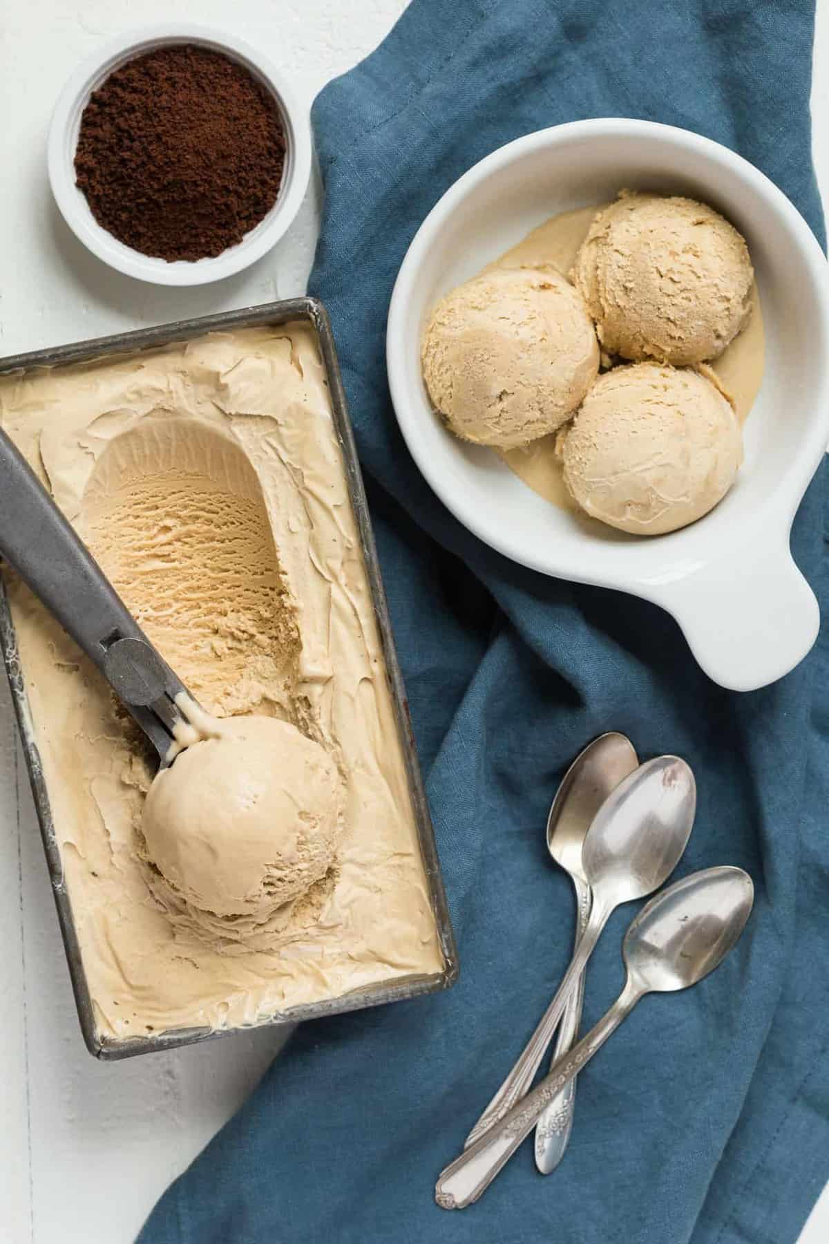 Homemade coffee ice cream being scooped out of a loaf pan into a white bowl.