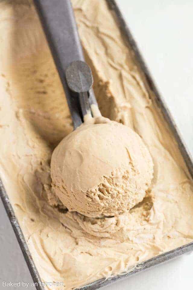 Creamy coffee ice cream in an ice cream scoop set over a pan of ice cream.