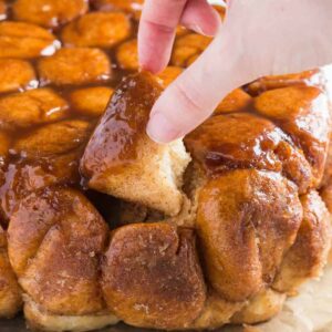 Slow Cooker Monkey Bread on a baking sheet lined with brown parchment paper and a hand taking out a piece of bread.