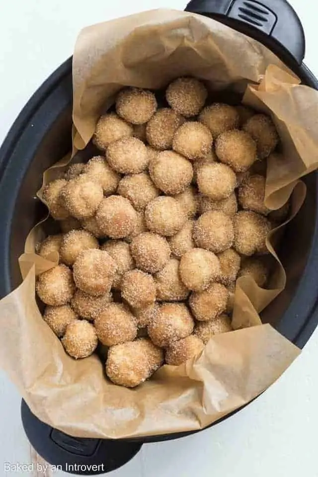 Overhead view of raw slow cooker monkey bread dough balls in a slow cooker lined with brown parchment paper.