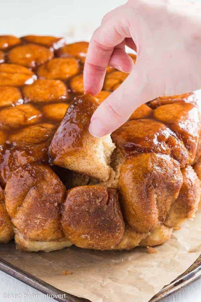 Slow Cooker Monkey Bread on a baking sheet lined with brown parchment paper and a hand taking out a piece of bread.