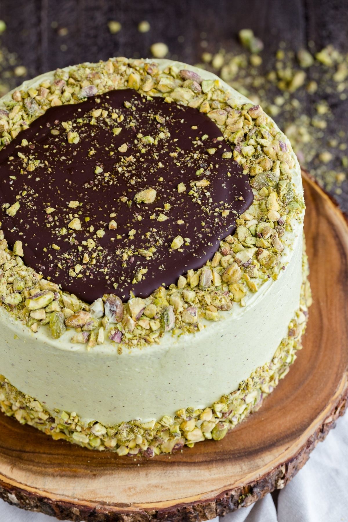 High-angled view of chocolate pistachio cake on a wooden cake stand.