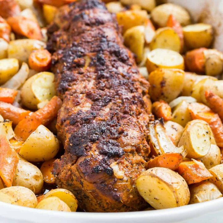 Angled view of Tomato Roasted Pork Loin with potatoes and carrots in a white casserole dish.