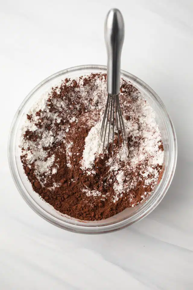 Flour and cocoa powder whisked in glass bowl.