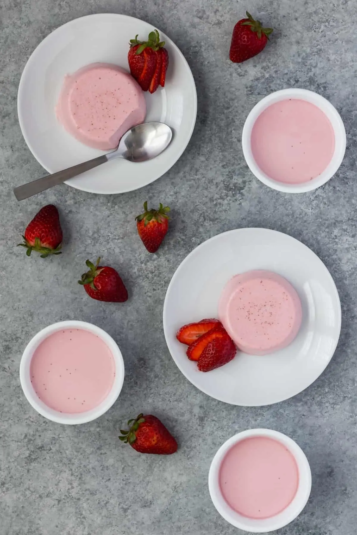 Two strawberry panna cottas on white plates and two in white ramekins.