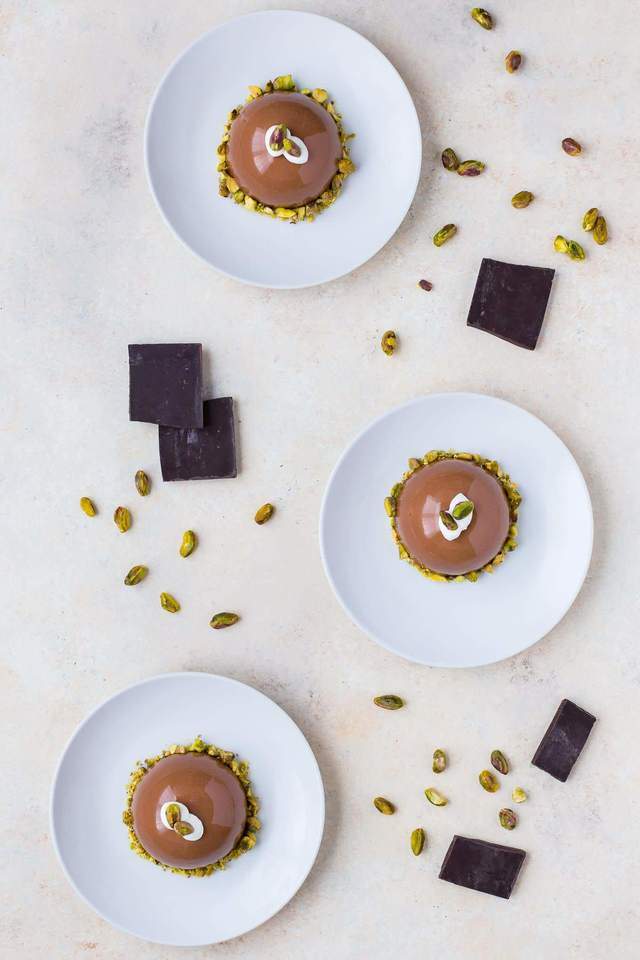 Overhead view of three chocolate pistachio domes on white plates.