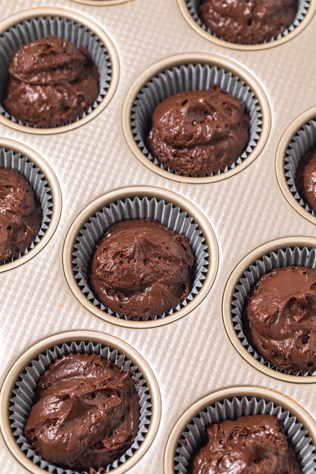 Chocolate cupcake batter in a lined muffin pan.