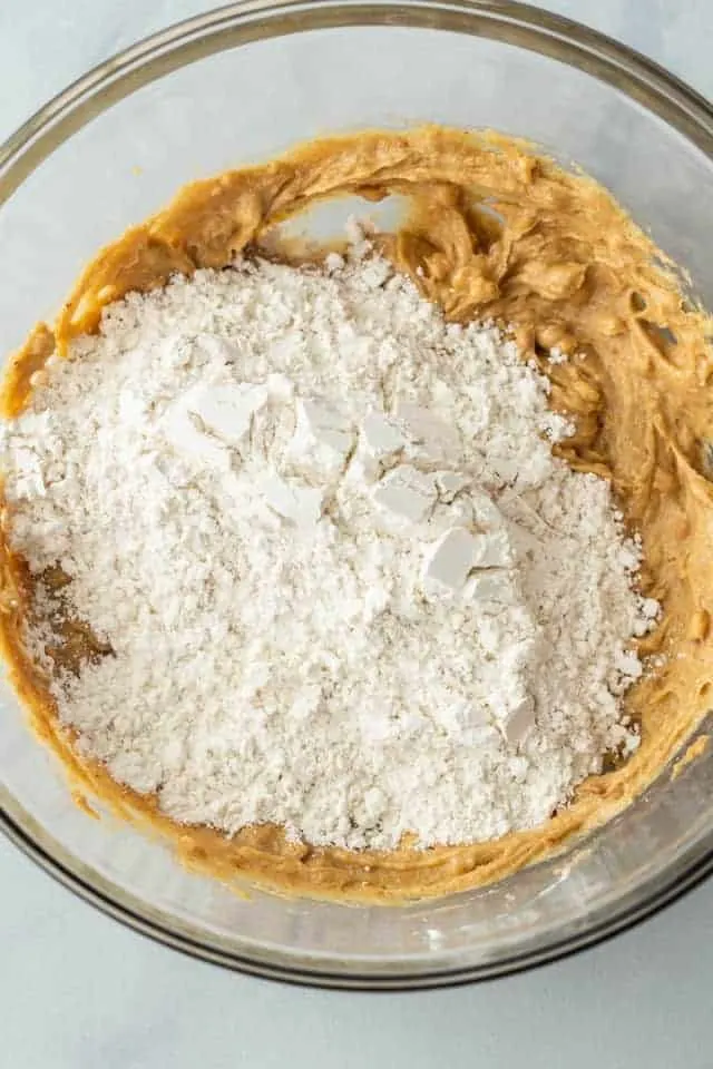 Flour added to wet ingredients in a glass bowl.