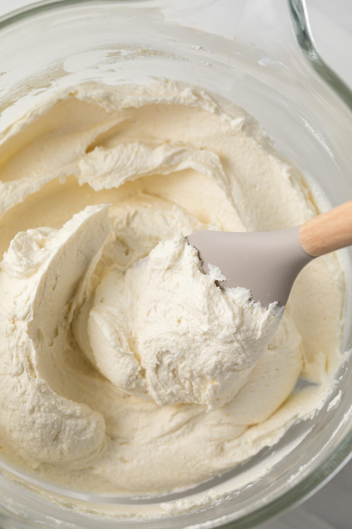 Pineapple frosting in a glass bowl with a spatula.