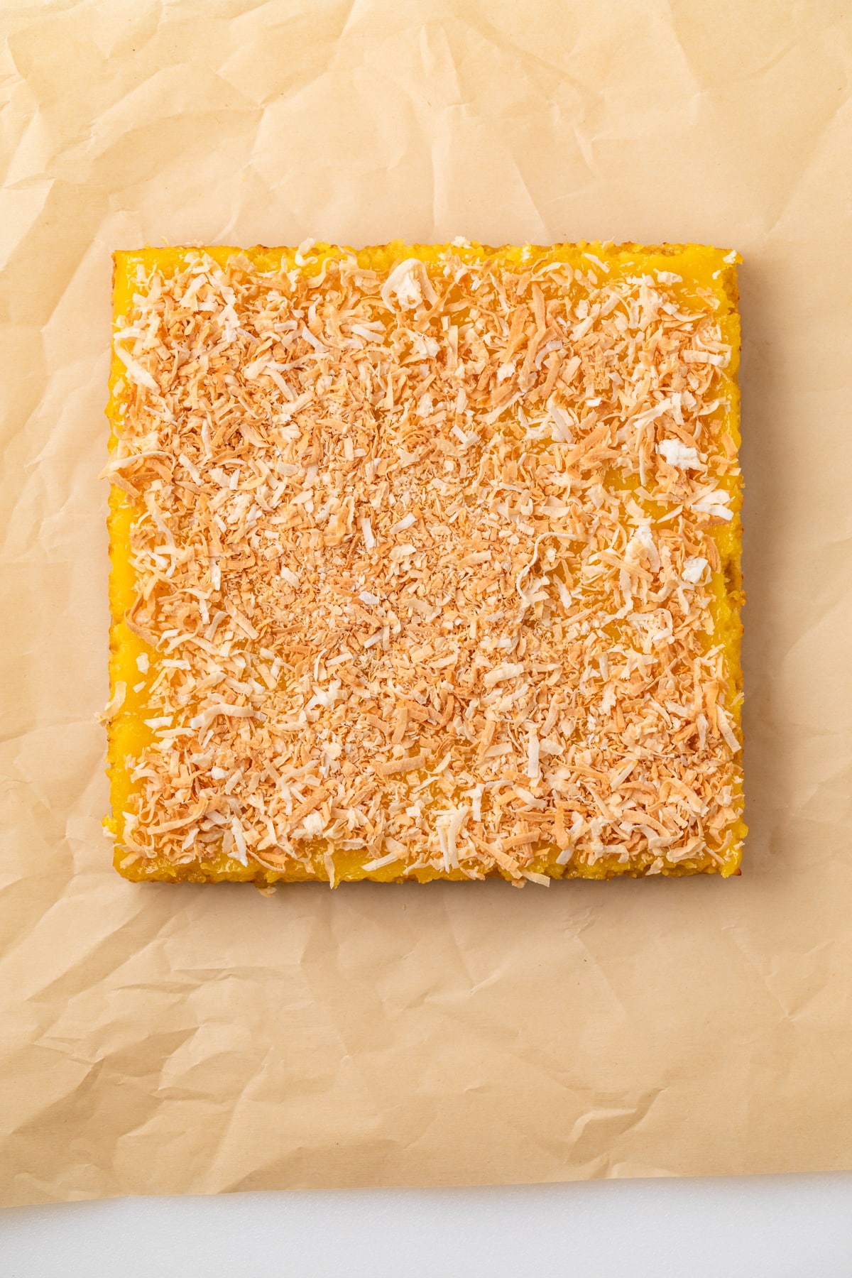 Coconut lemon bars uncut on parchment paper.
