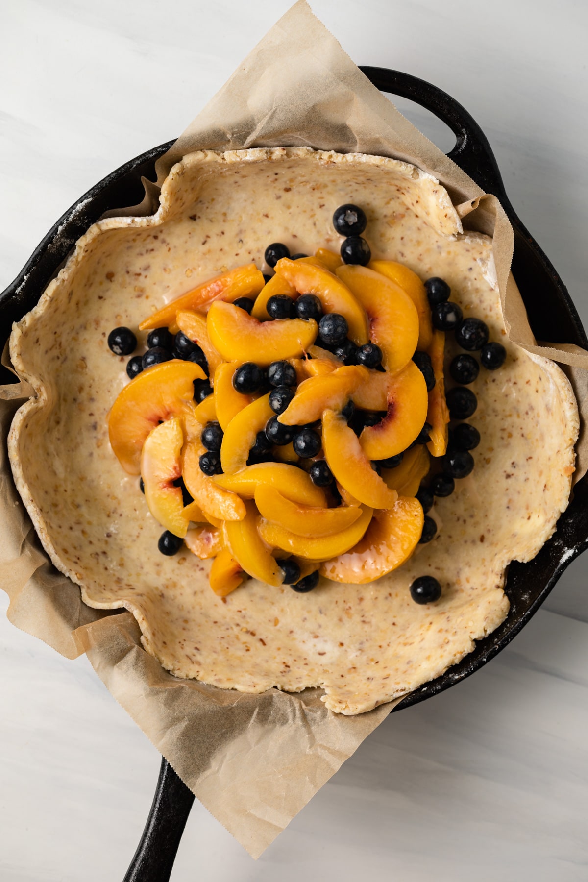 Peaches and blueberries in pastry dough in cast iron skillet.