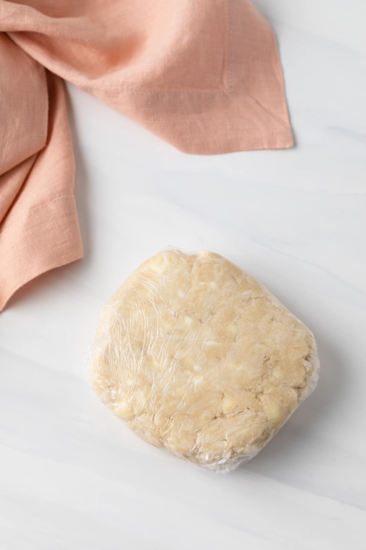homemade pie crust dough shaped into a disk and wrapped in plastic wrap
