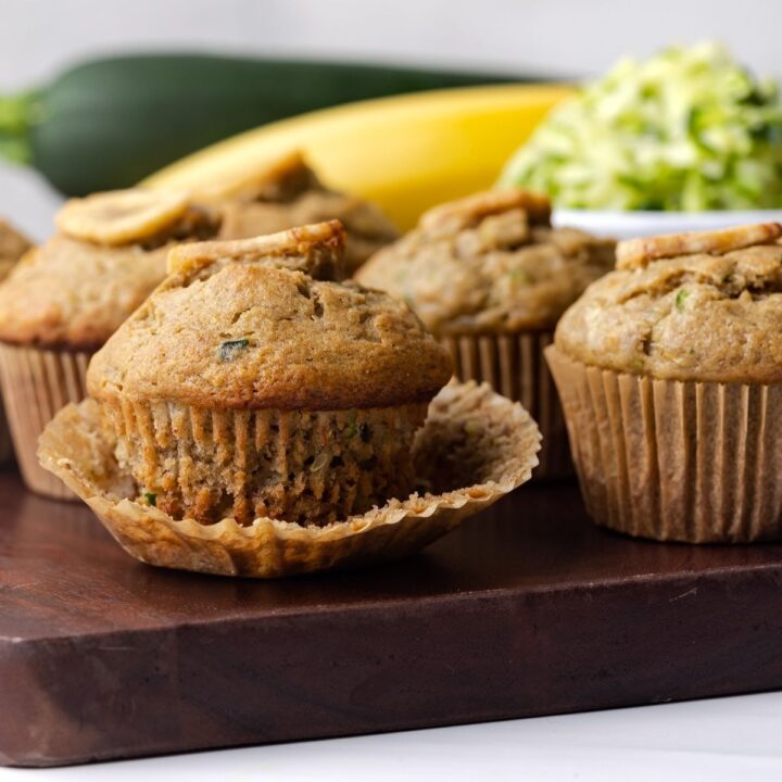Zucchini muffins on wooden board with the wrapper peeled away from the one in front.