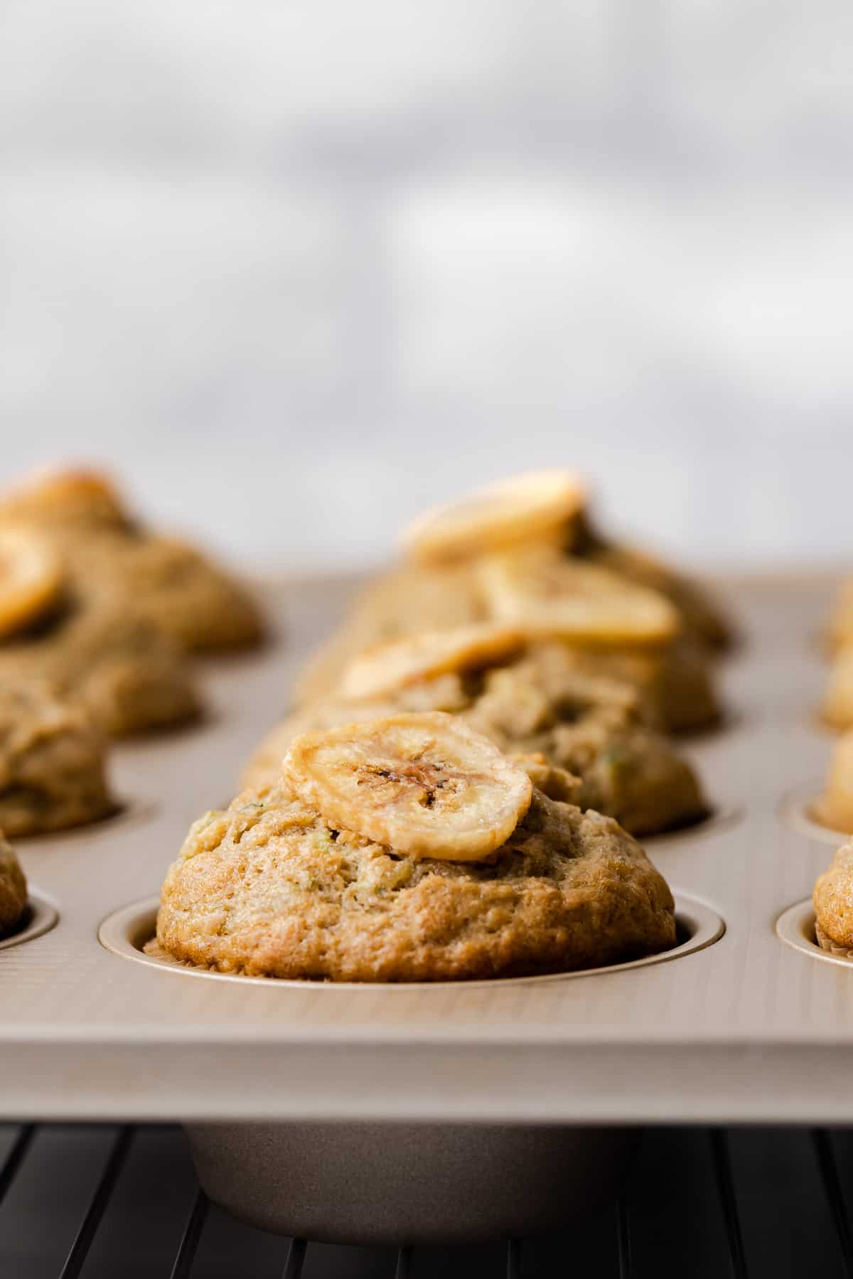 Zucchini banana muffins topped with banana chips on a muffin pan.